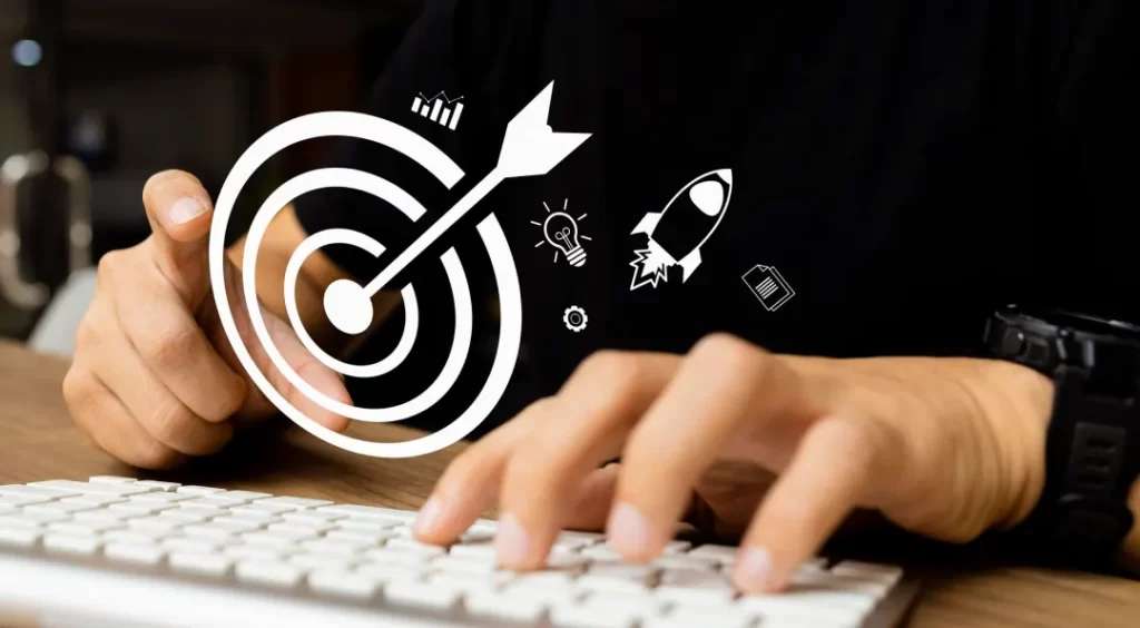 Mãos digitando em um teclado branco, com uma superposição digital de um alvo com uma flecha e ícones relacionados a metas e ideias flutuando sobre a imagem.