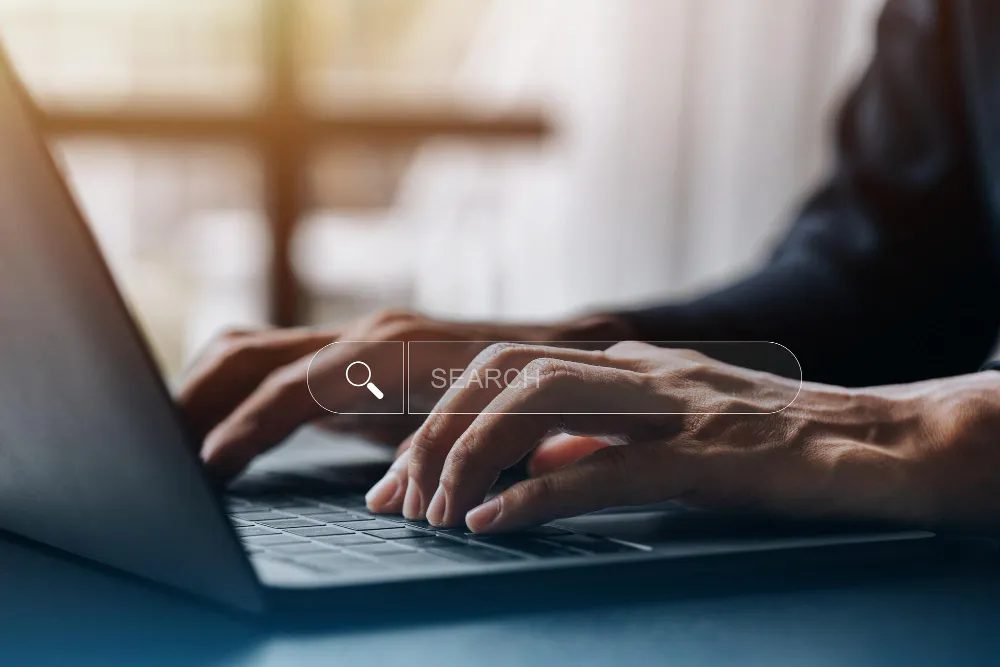 Homem digitando em um laptop com uma barra de pesquisa flutuante sobreposta à imagem, com a palavra "SEARCH" dentro dela.