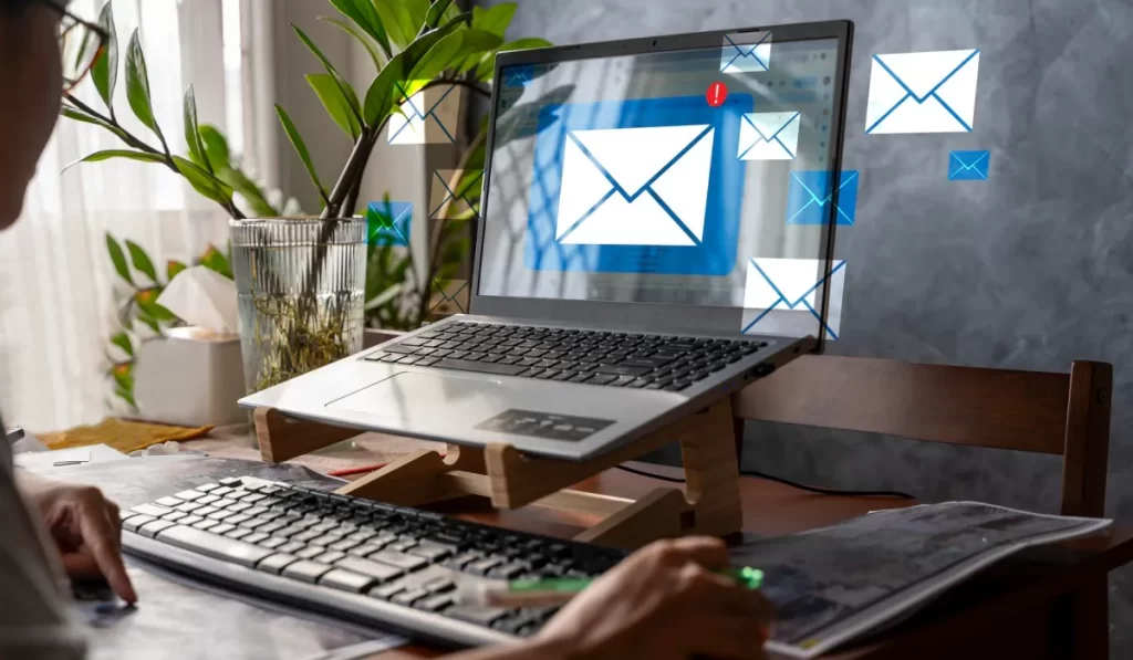 Pessoa utilizando notebook com diversas notificações de e-mail representadas graficamente na tela.