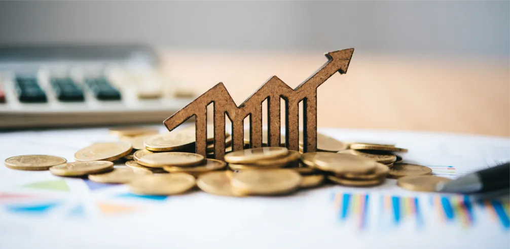 Moedas empilhadas ao redor de um ícone de gráfico de crescimento com seta para cima, representando aumento financeiro ou crescimento econômico.